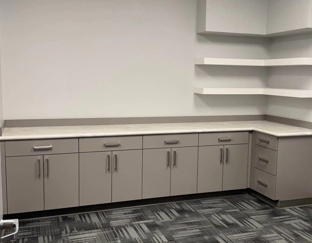Commercial break room with a taupe cabinet run, quartz countertop and white floating corner shelves