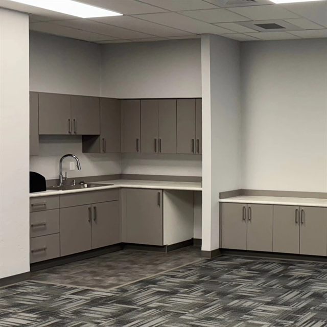 Commercial office kitchenette with taupe slab-front casework and corner desk return
