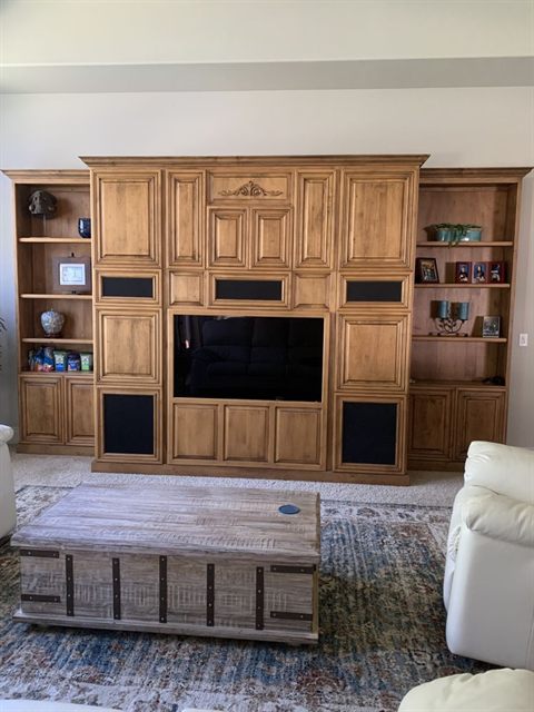 Floor-to-ceiling stained oak entertainment center with open display shelving either side of a television opening
