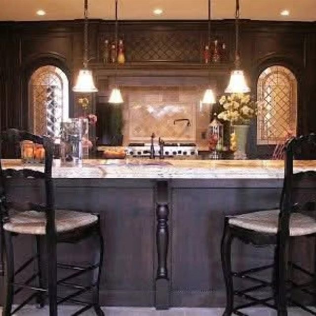 Dark-stained traditional cabinets with arched open display niches above a tumbled stone backsplash