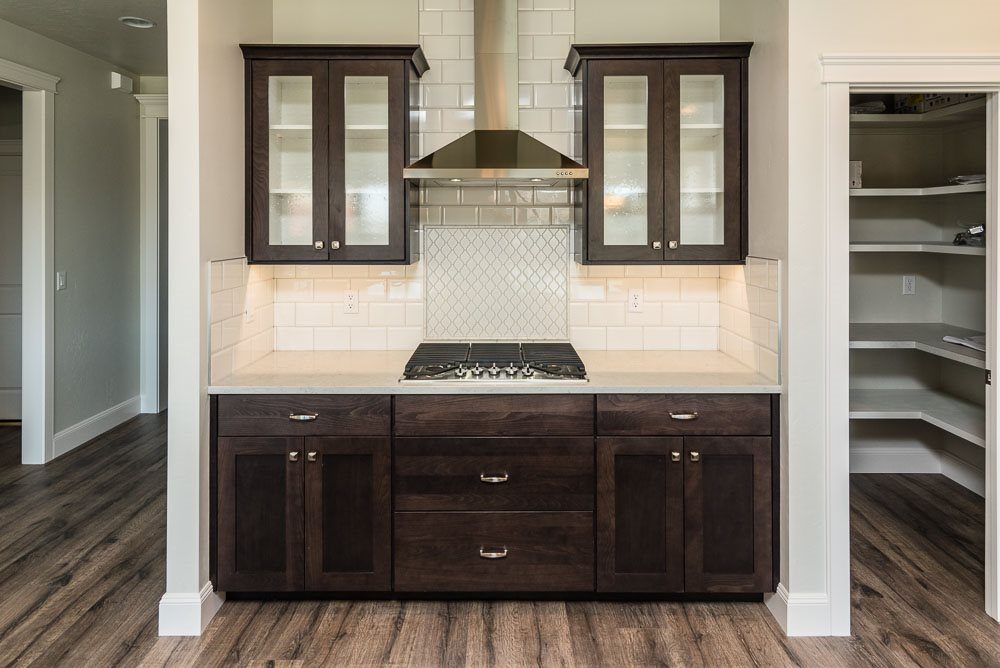 Custom kitchen with espresso-stained base cabinets, glass-front upper cabinets, a herringbone tile backsplash and a walk-in pantry with fitted shelving