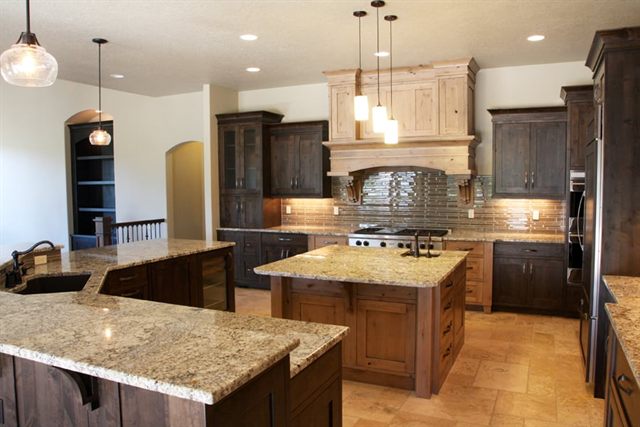 Open-plan custom kitchen with a large granite-topped island, two-tone cabinetry, a built-in wood range hood and pendant lighting